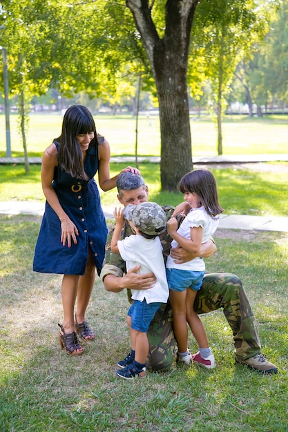 Glückliche Mutter und zwei Kinder, die militärischen Vater in Tarnuniform im Freien umarmen. Vertikaler Schuss. Familientreffen oder Rückkehr nach Hause Konzept
