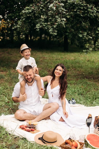 Glückliche Mutter, Vater und ihr süßer kleiner Sohn haben ein Picknick im Sommerpark. Kind sitzt auf den Schultern seines Vaters. Familien- und Freizeitkonzept