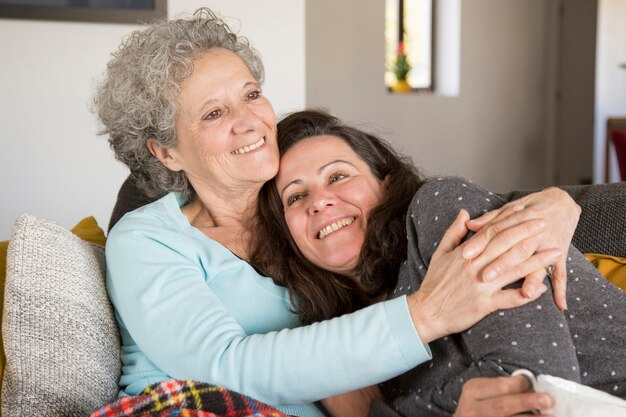 Glückliche nachdenkliche ältere Dame, die zu Hause ihre Tochter umfasst