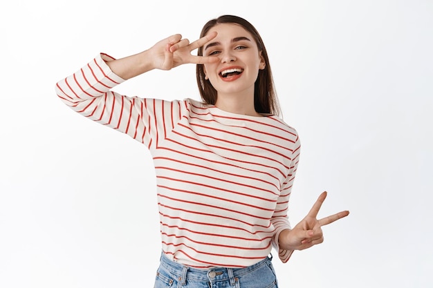 Glückliche positive Frau, die mit Friedens-V-Zeichen tanzt und fröhlich lacht, Freizeitwochenenden genießt, fröhlich vor weißem Hintergrund posiert