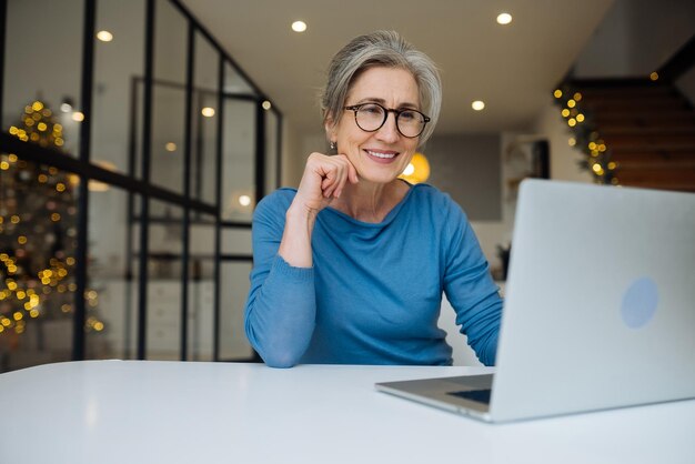 Glückliche reife ältere Frau mittleren Alters, die gute Nachrichten liest und auf den Laptop schaut