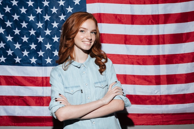 Glückliche rothaarige junge Dame, die über USA-Flagge steht