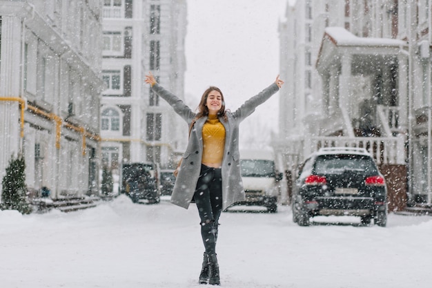 Glückliche schneiende Winterzeit in der Großstadt des hübschen Mädchens, das Schneefall auf Straße genießt. Wahre positive Emotionen, Händchen haltend,
