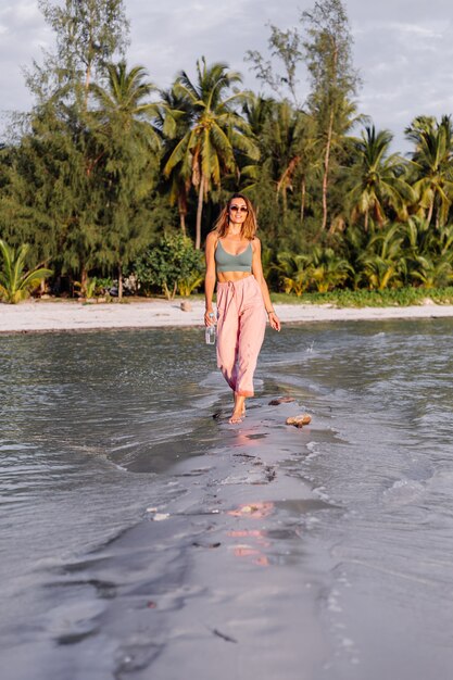 Glückliche schöne junge europäische Frau mit Plastikflasche Wasser in ihrer Hand im Strand