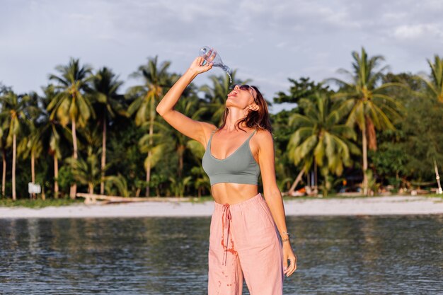 Glückliche schöne junge europäische Frau mit Plastikflasche Wasser in ihrer Hand im Strand