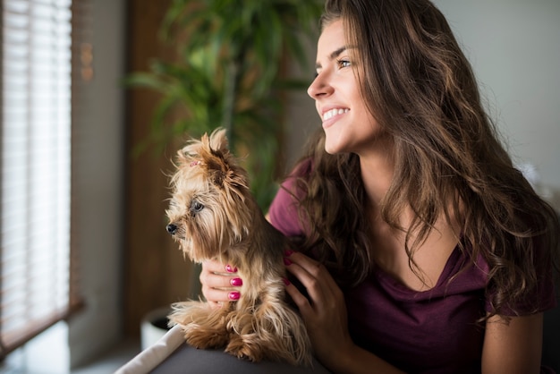 Glückliche schöne junge Frau, die Fenster mit ihrem Hund betrachtet