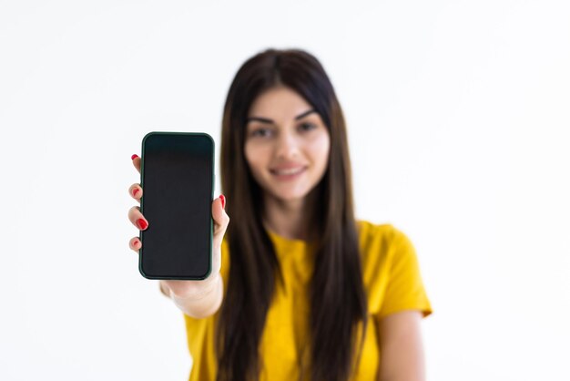 Glückliche schöne junge Frau, die Handy des leeren Bildschirms hält und Finger über weißen Hintergrund zeigt