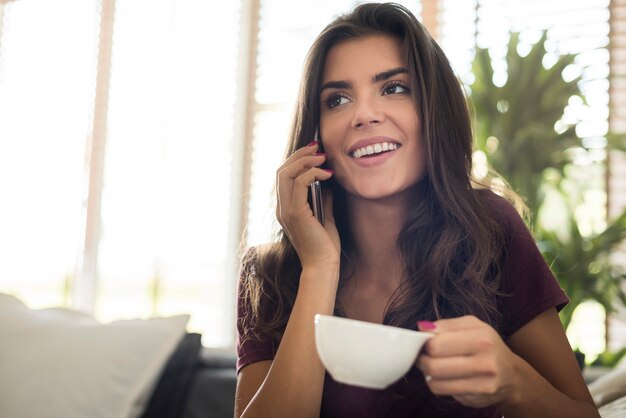 Glückliche schöne junge Frau mit Kaffeetasse und Telefonieren