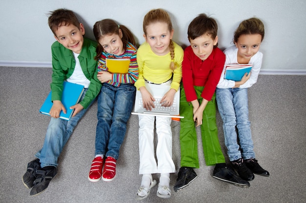 Glückliche Schüler in einer Reihe auf dem Boden sitzen