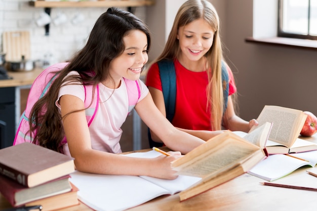 Glückliche Schulmädchen mit den Rucksäcken, die am Schreibtisch sitzen und im Klassenzimmer trainieren