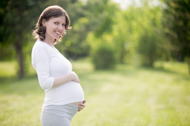 Glückliche schwangere Frau auf späte Schwangerschaft Bühne posiert im Park