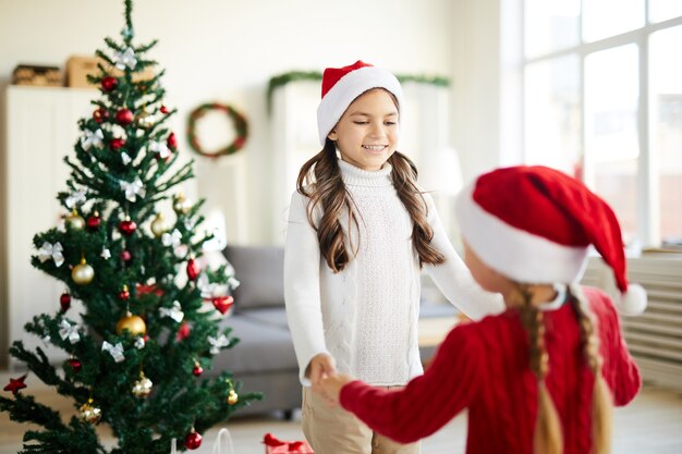 Glückliche Schwestern tanzen und spielen neben dem Weihnachtsbaum