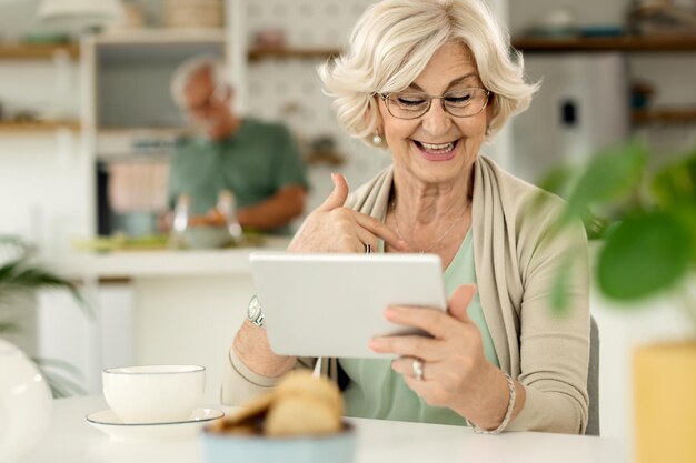 Glückliche Seniorin, die zu Hause einen Videoanruf über das Touchpad tätigt