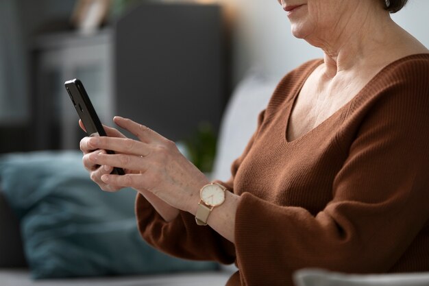 Glückliche Seniorin mit Smartphone im Wohnzimmer einer modernen Wohnung