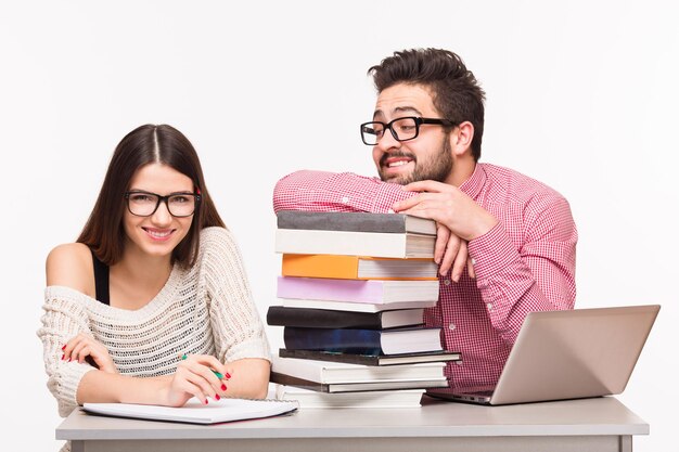 Glückliche Studenten, die am Tisch sitzen und sich auf Prüfungen vorbereiten. Glückliche Dame, die in die Kamera schaut, und ihr Gruppenkamerad, der sie ansieht.