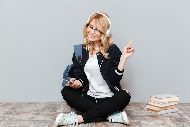 Glückliche studentin, die musik auf dem boden hört