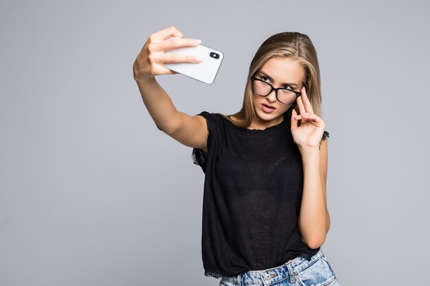 Glückliche süße Frau, die selfie am Telefon über grauem Hintergrund macht.