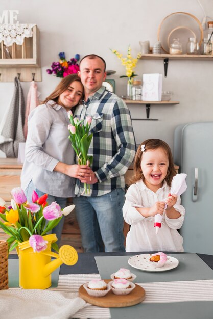 Glückliche Tochter, die kleinen Kuchen nahe Eltern mit Blumen macht