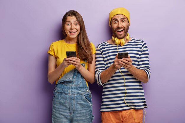 Glückliche überglückliche junge Leute senden Textnachrichten, die von modernen Technologien abhängig sind