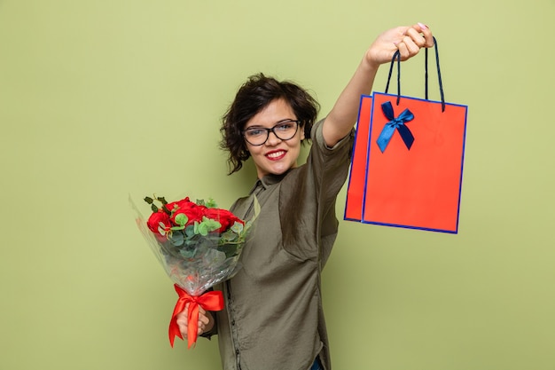 Glückliche und positive Frau mit dem kurzen Haar, das Blumenstrauß und Papiertüte mit Geschenken hält, die fröhlich feiern, den internationalen Frauentag 8. März feiern