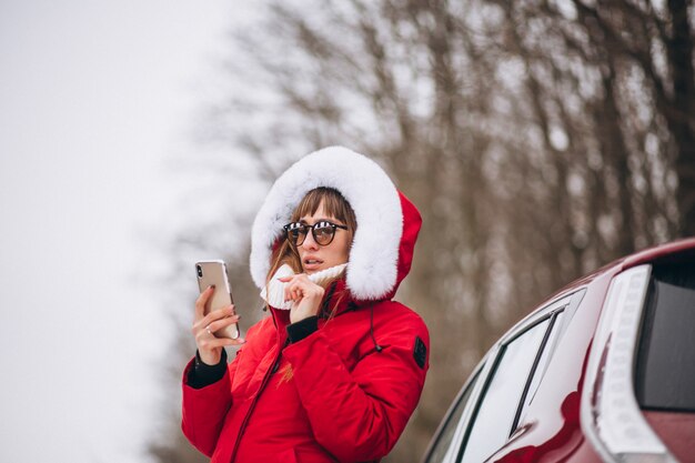 Glückliche Unterhaltung der Frau am Telefon draußen mit dem Auto im Winter