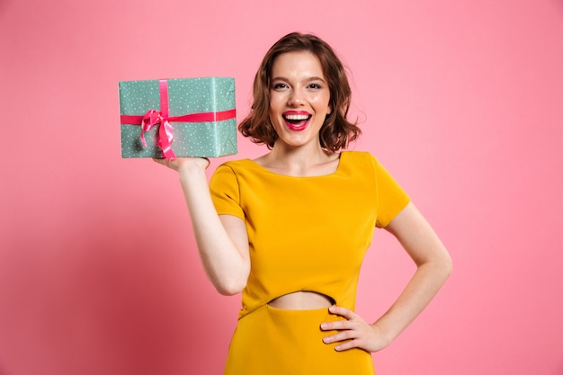 Glückliche ypung Frau mit Hand auf ihrer Taille, die Geschenkbox hält,