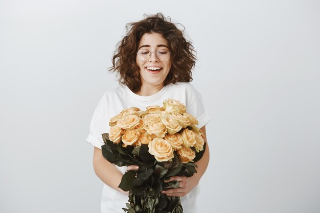 Glückliche zarte Freundin erhalten Blumenstrauß von schönen Blumen, hält Rosen und seufzt erstaunt