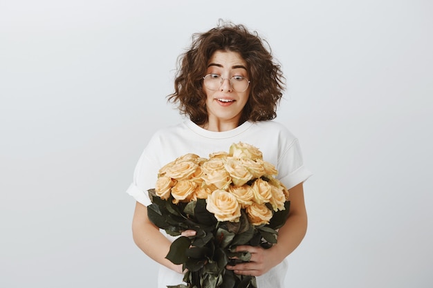 Glückliche zarte freundin erhalten blumenstrauß von schönen blumen, hält rosen und seufzt überrascht