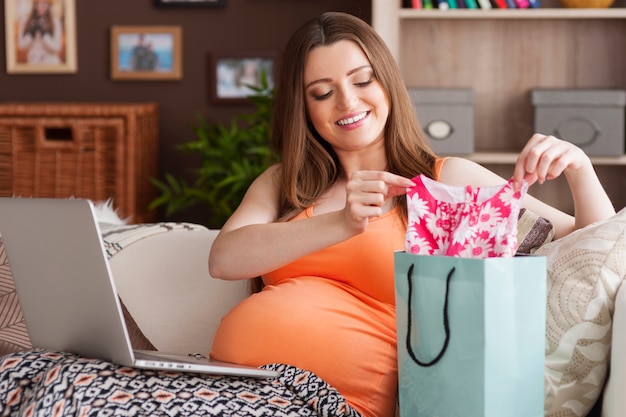 Glückliche zukünftige Mutter, die Kleidung für kleines Mädchen vorbereitet