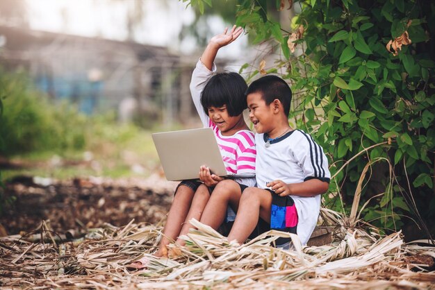 Glückliche zwei asiatische Kinder, die einen Laptop für das E-Learning zu Hause in einer entfernten Schule im Landesinneren verwenden