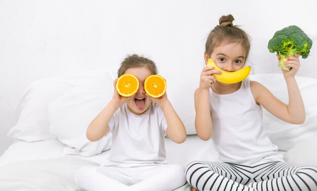 Glückliche zwei niedliche Kinder, die mit Obst und Gemüse spielen.