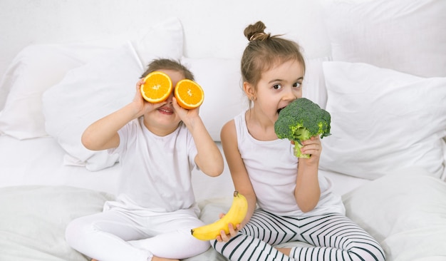 Glückliche zwei niedliche Kinder, die mit Obst und Gemüse spielen.