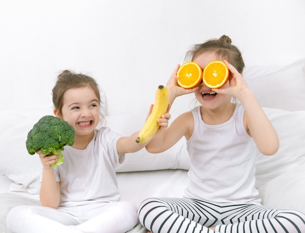 Glückliche zwei niedliche Kinder spielen mit Obst und Gemüse auf einem hellen Hintergrund. Gesundes Essen für Kinder.