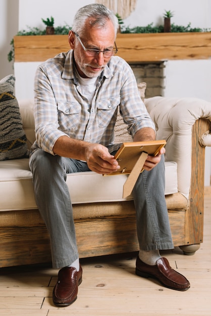 Glücklicher älterer Mann, der auf dem Sofa betrachtet Fotorahmen sitzt