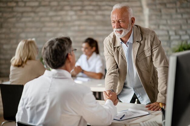 Glücklicher älterer Mann, der nach Konsultationen in der Klinik einem Arzt die Hand schüttelt