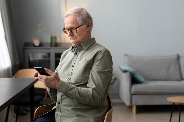 Glücklicher älterer Mann mit Smartphone im Wohnzimmer einer modernen Wohnung