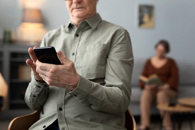 Glücklicher älterer Mann mit Smartphone im Wohnzimmer einer modernen Wohnung
