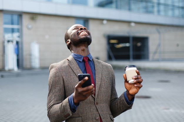 Glücklicher Afroamerikanermann schaut glückliches etwas in seinem Smartphone lesend