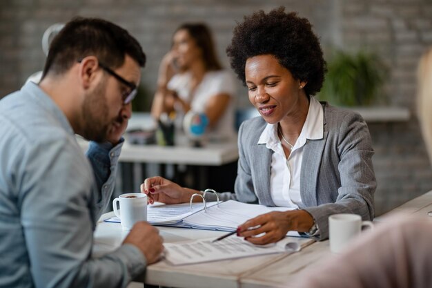 Glücklicher afroamerikanischer Bankmanager, der während des Treffens im Büro die Vertragsbedingungen mit ihrem Kunden analysiert