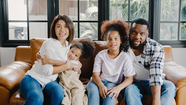 Glücklicher afroamerikanischer Familienvater, Mutter und Tochter, die Spaß beim Kuscheln und Videoanruf auf dem Laptop auf dem Sofa im Haus haben.