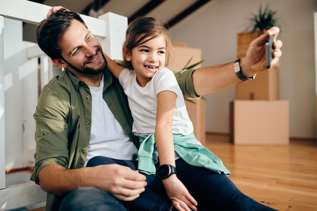 Glücklicher alleinerziehender Vater und seine Tochter, die nach dem Umzug in ein neues Zuhause ein Selfie machen