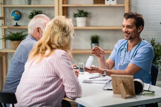 Glücklicher Arzt, der eine Tablettenflasche hält, während er mit einem älteren Paar über die Vitamine spricht, die sie einnehmen sollten