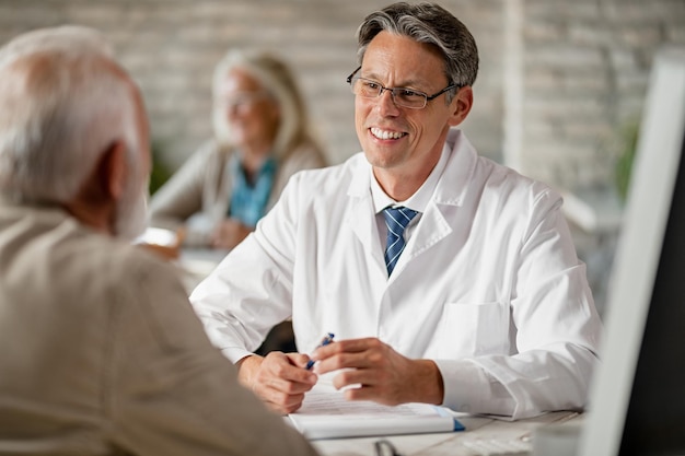 Glücklicher Arzt, der einen älteren Patienten während der Konsultationen in der Klinik über Krankenversicherungsmöglichkeiten informiert