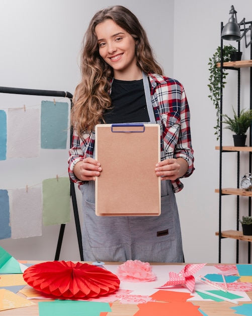 Glücklicher attraktiver weiblicher Künstler, der Klemmbrett mit normalem braunem Papier zeigt