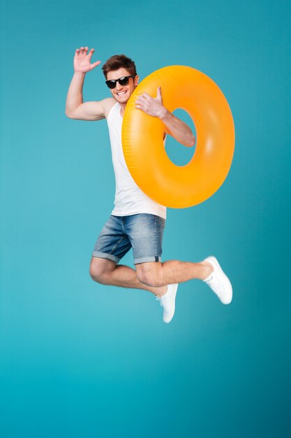 Glücklicher aufgeregter Mann in der Sonnenbrille, die aufblasbaren Ring hält und springt