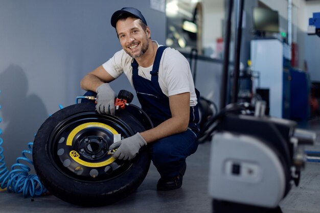 Glücklicher Automechaniker, der den Druck in einem Reifen überprüft, während er in der Werkstatt arbeitet