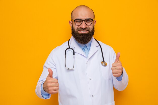Glücklicher bärtiger Arzt im weißen Kittel mit Stethoskop um den Hals mit Brille, der fröhlich lächelt und Daumen nach oben zeigt