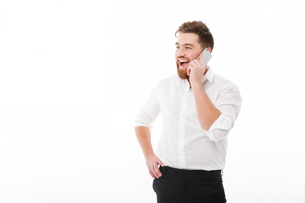 Glücklicher bärtiger Mann in der Geschäftskleidung sprechend durch Smartphone