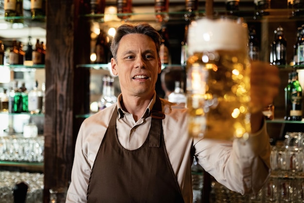 Glücklicher Barkeeper, der ein Glas Bier vom Fass hält, während er in einer Bar arbeitet.