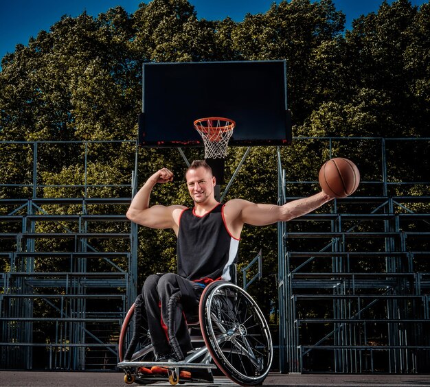 Glücklicher Basketballspieler in einer Rollstuhlpose mit einem Ball auf offenem Spielfeld.